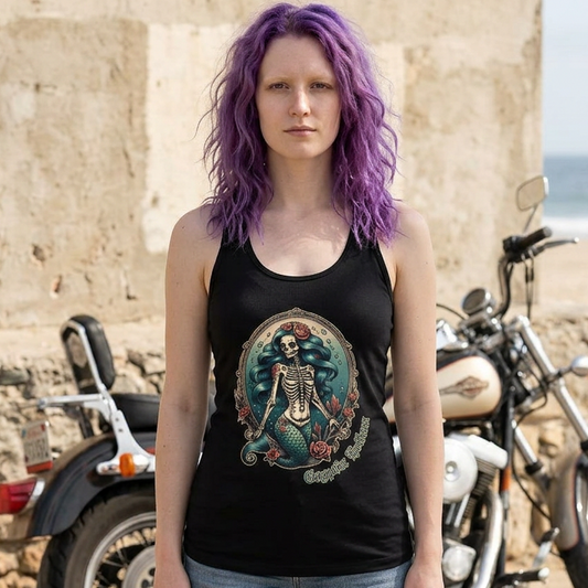 Woman with purple hair wearing a black tank top with a skeleton mermaid design, standing in front of a motorcycle.
